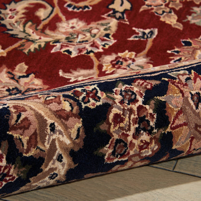 Close-up of a red oriental rug with a navy border and cream floral motifs, showing a folded edge on a wooden floor.