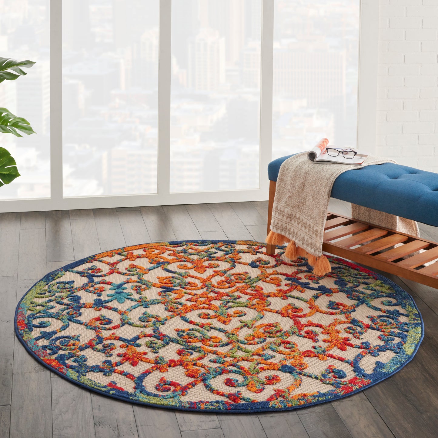 Round area rug with vibrant multicolor floral scroll pattern in red, blue, green and orange on a light background.