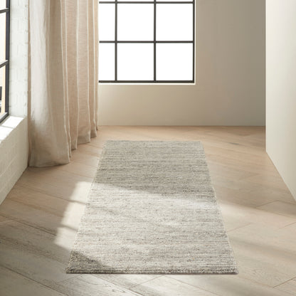 Light gray woven rug runner on pale wood floor, in a bright room with large grid window and beige curtains.