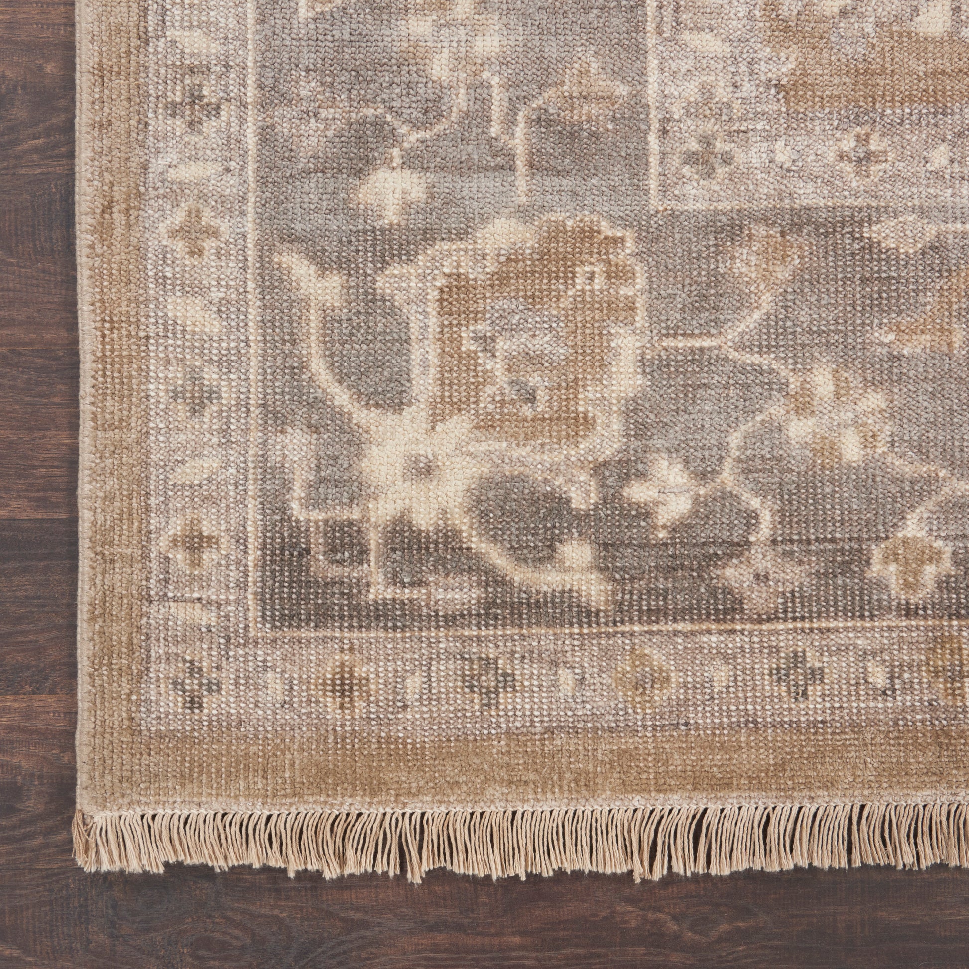 Neutral-toned oriental rug with cream, beige and taupe floral motif, fringed border on dark wood floor.