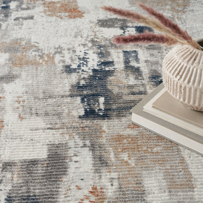 Blue-beige abstract rug in neutral tones, with a cream ribbed ceramic vase containing pampas grass atop neutral stacked books.