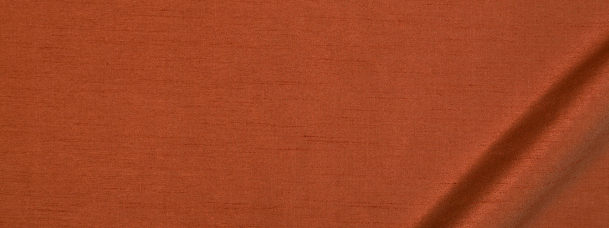 Close-up of burnt-orange fabric with visible weave and soft crease.