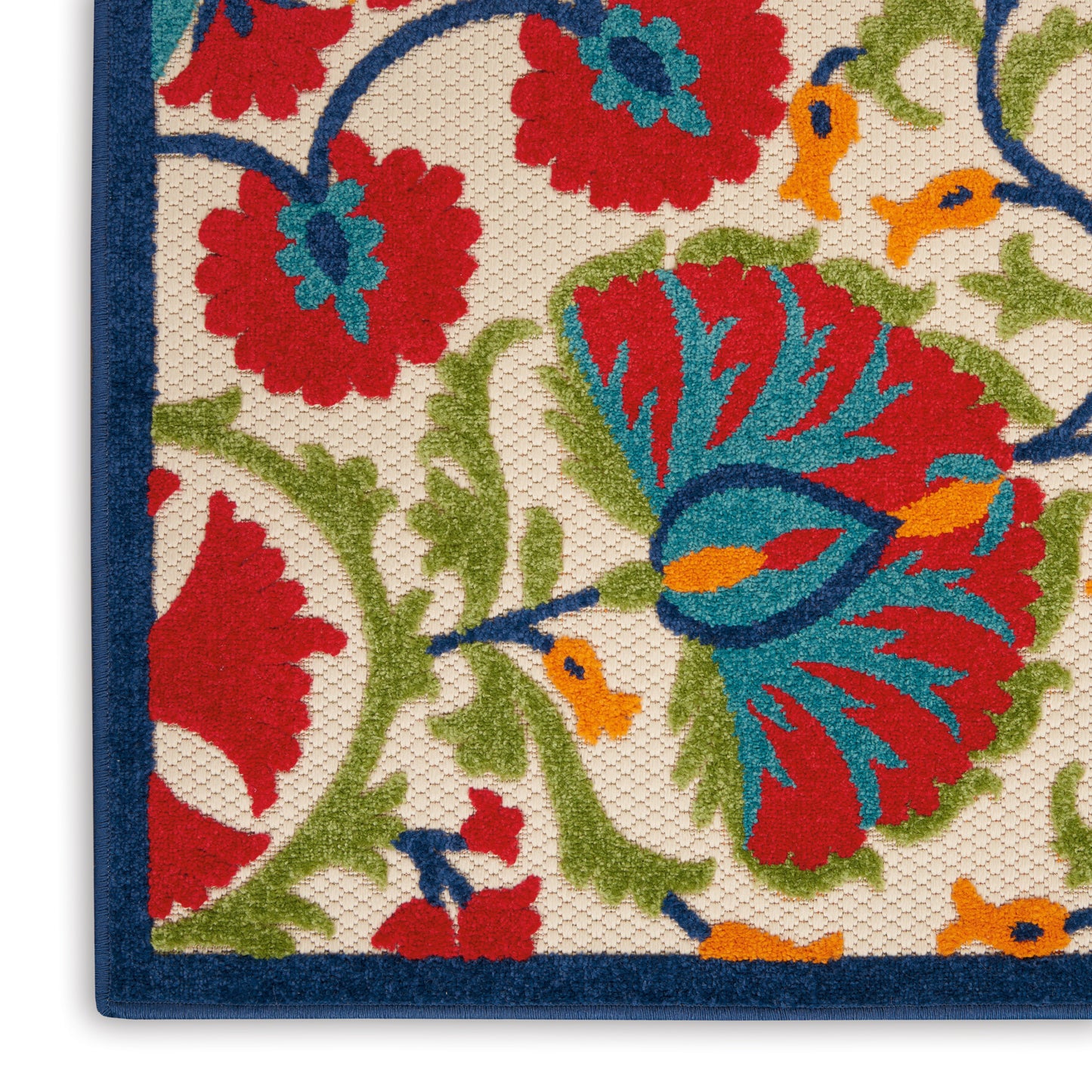 Woven floral area rug corner with cream background, bold red and teal flowers, green vines, and a dark blue border.
