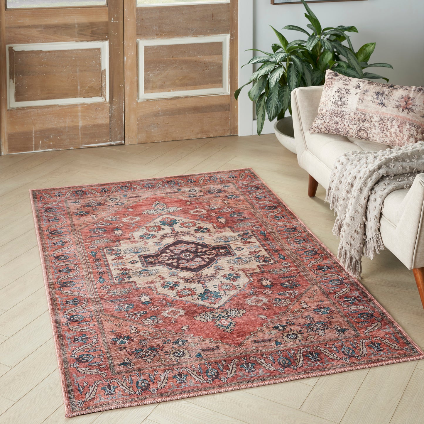 Red oriental area rug with ivory & blue medallion motif on light wood floor beside a beige sofa.