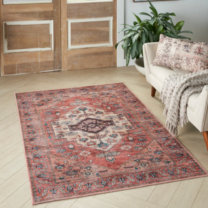 Red oriental area rug with ivory & blue medallion motif on light wood floor beside a beige sofa.