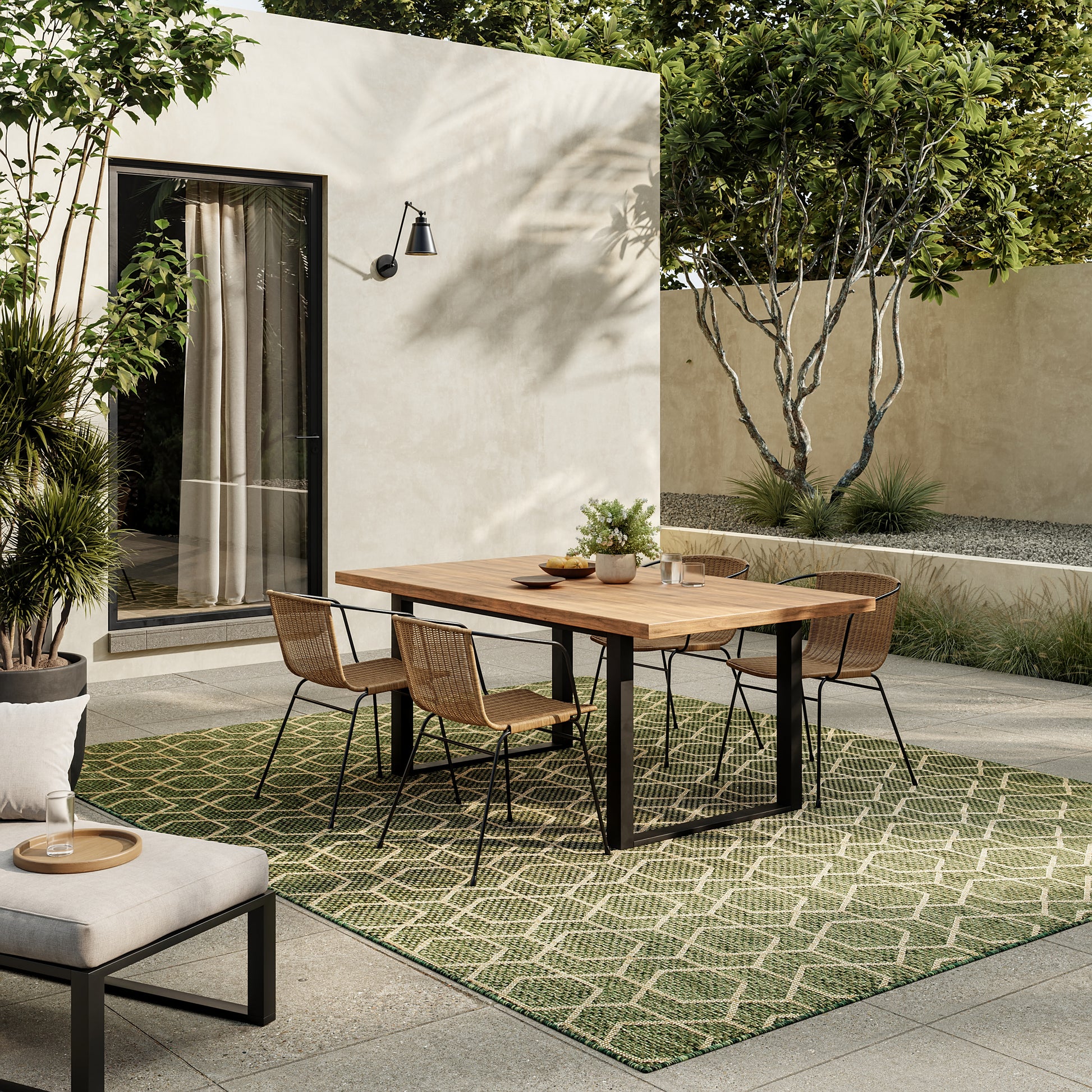 Patio dining set with wooden table, black metal legs, wicker chairs, on a green rug beside beige stucco wall.
