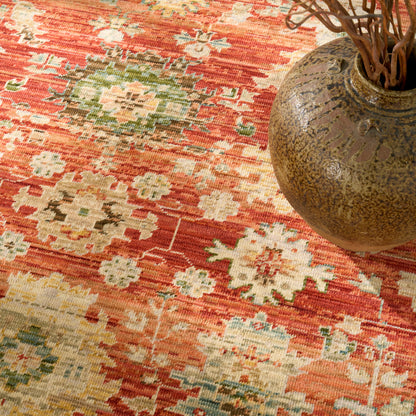Vintage 6' x 9' orange-red oriental rug with ivory and sage floral motifs; round brown ceramic vase with twigs in corner.