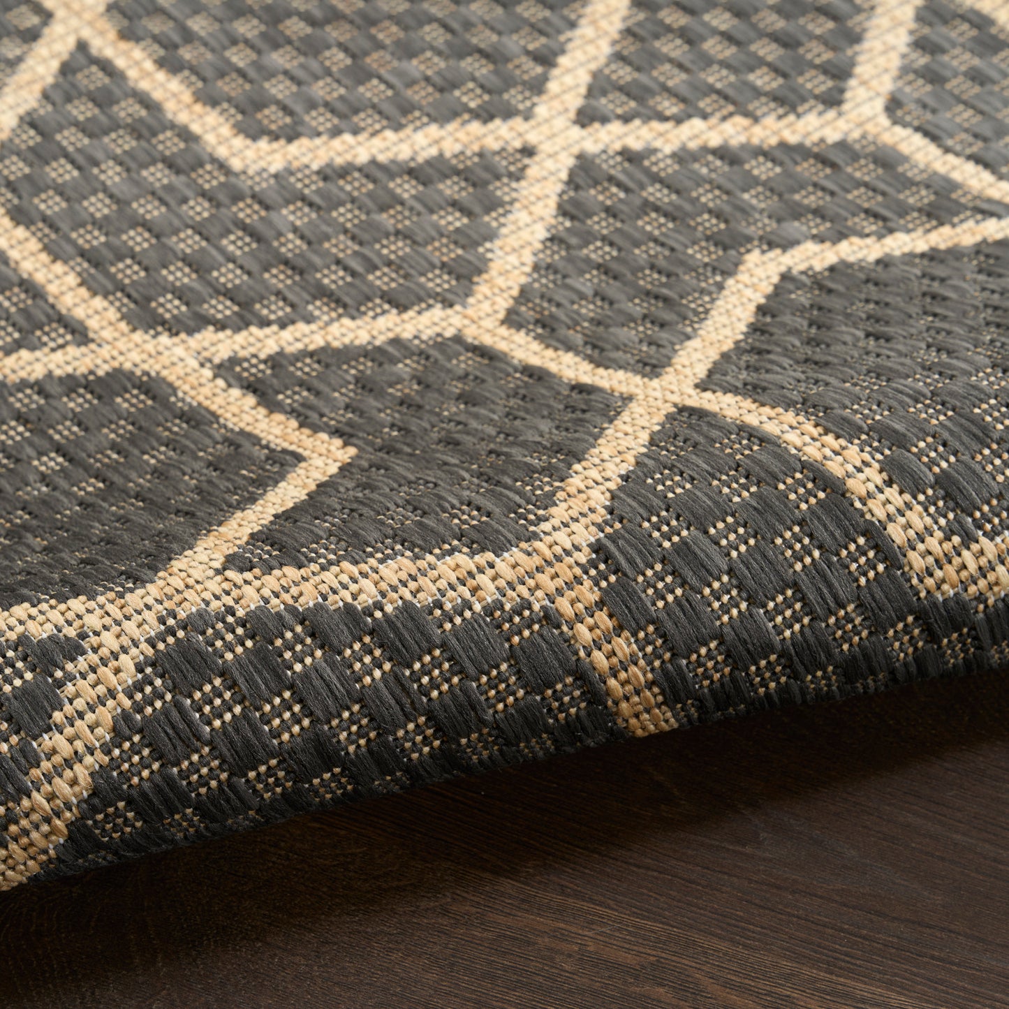 Dark gray flatweave rug with beige geometric lattice pattern and border, modern living room decor.