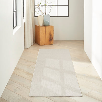 Light beige hallway runner rug on pale wood flooring with a wooden block side table and vases by a window.