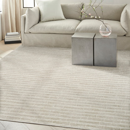 Neutral living room with light beige sofa, textured rug, concrete cube side tables, and glass vase with blossoming branches.