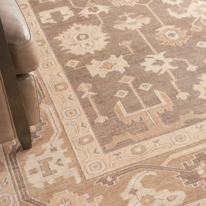 Beige oriental area rug with cream geometric floral motifs beside a brown leather sofa.