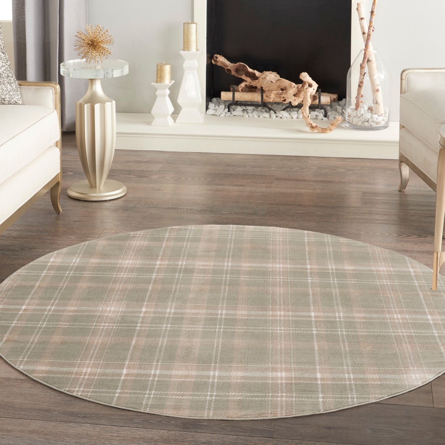 Round plaid rug in soft greens & beige with pink accents; cozy living room with wood floor & neutral furniture.