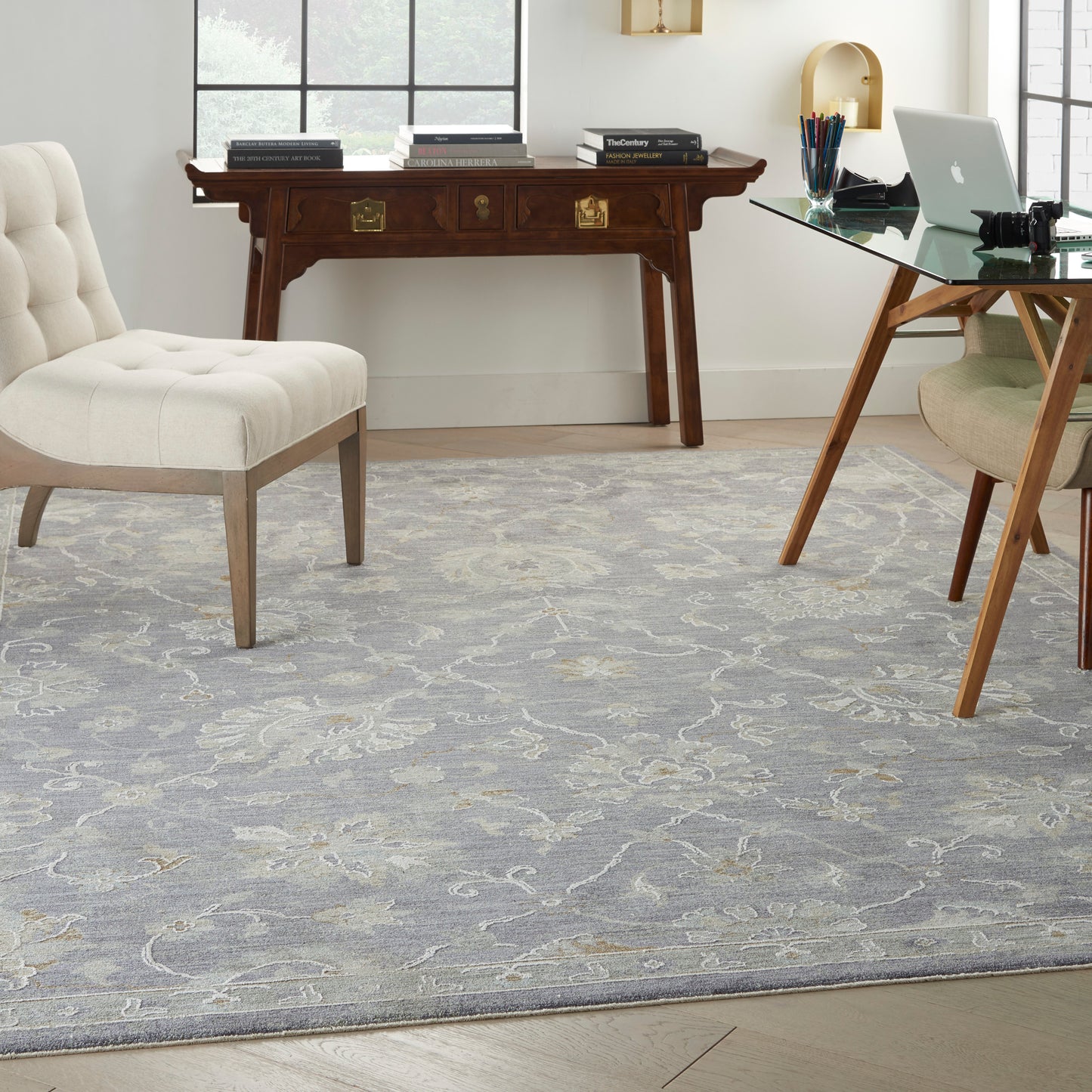 Light gray patterned rug, beige tufted chair, glass-top desk with laptop, and dark wood writing desk in a bright home office.