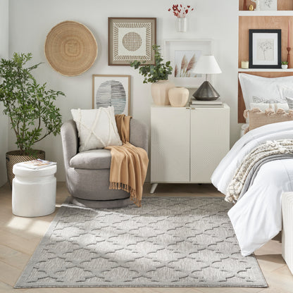 Cozy bedroom scene with gray armchair, beige throw, white cabinet, framed art, plants, and a light gray geometric rug.