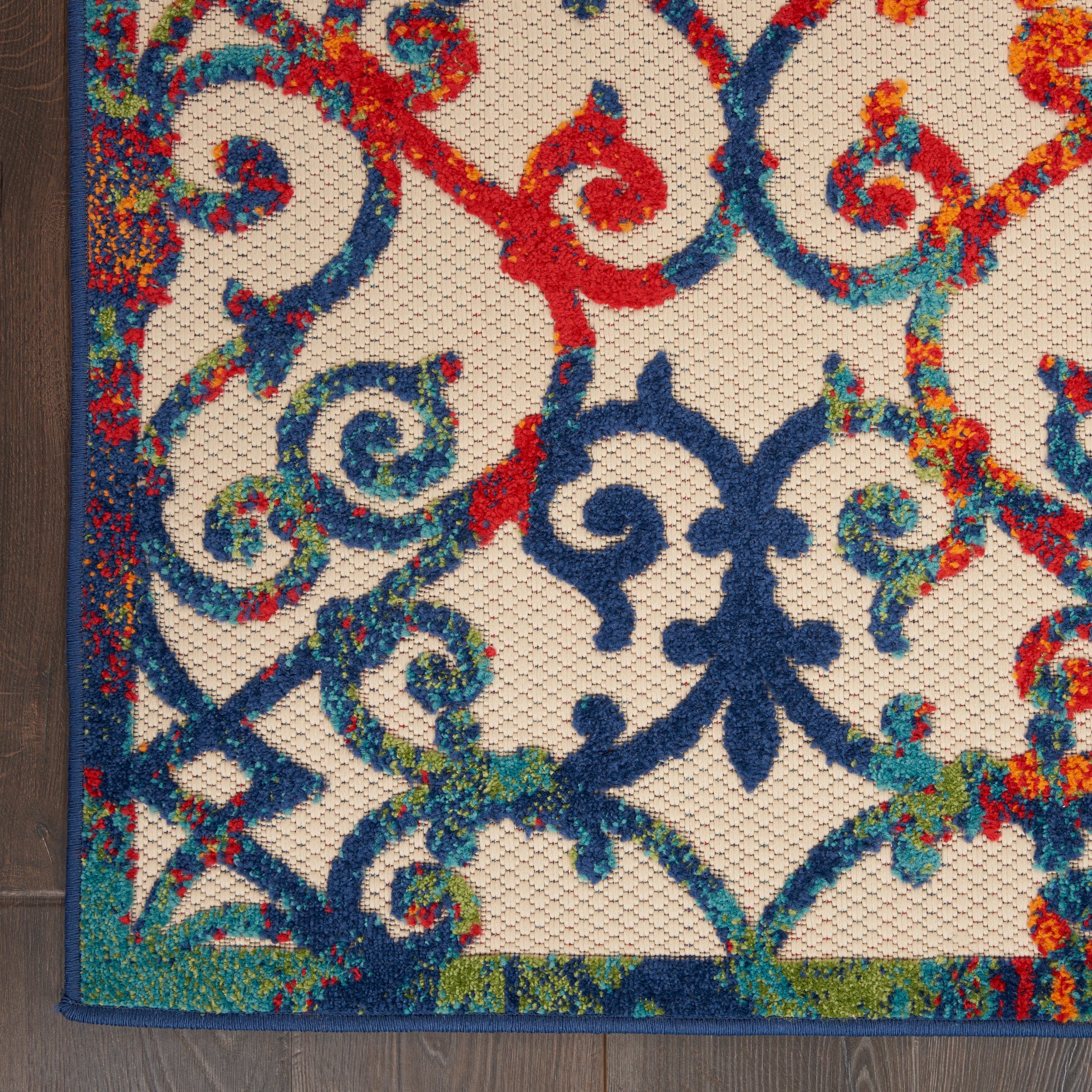 Colorful ornate tufted rug with blue, teal, red scrolling motifs on beige background; blue border.
