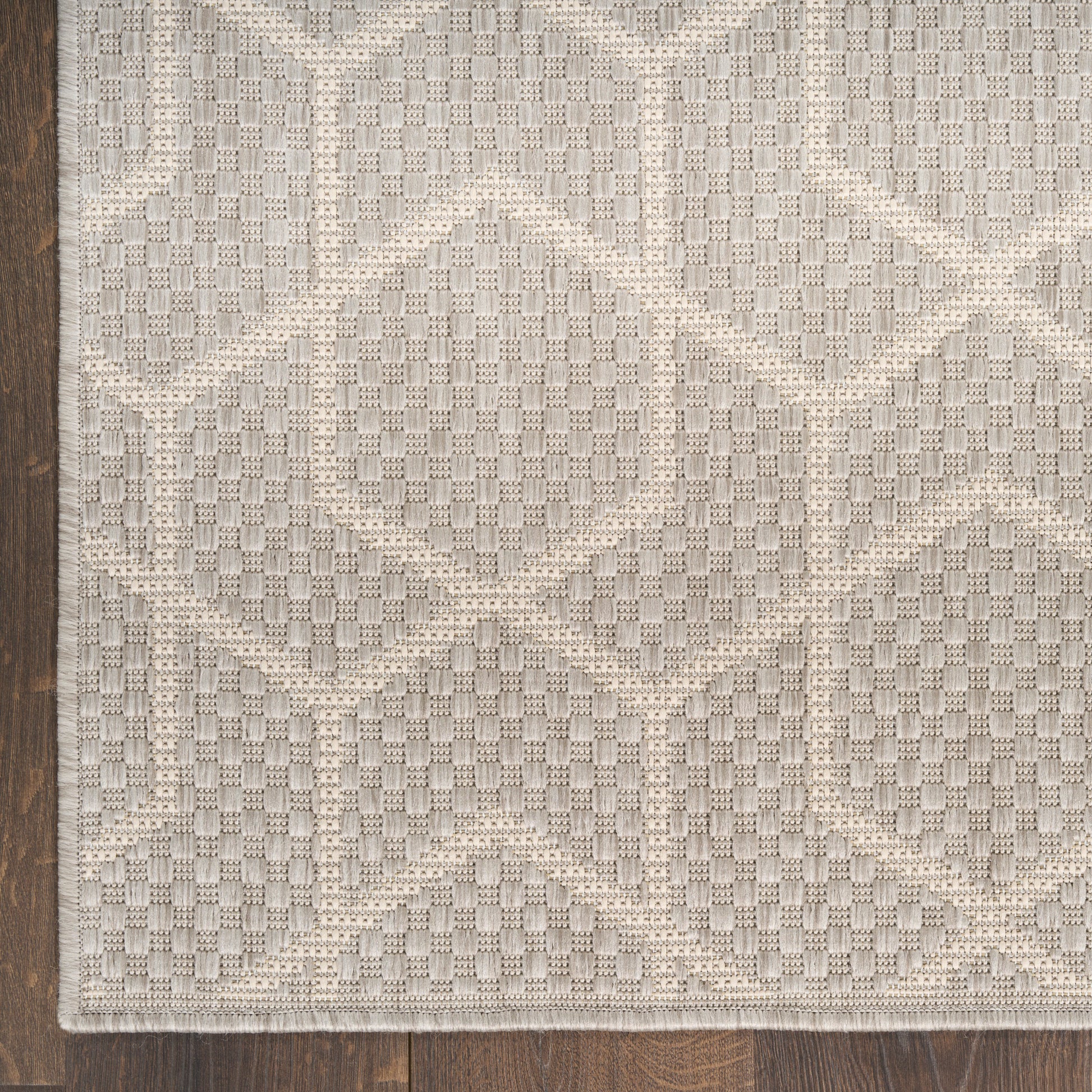 Beige and cream geometric rug with diamond motif and textured weave on dark wood floor.