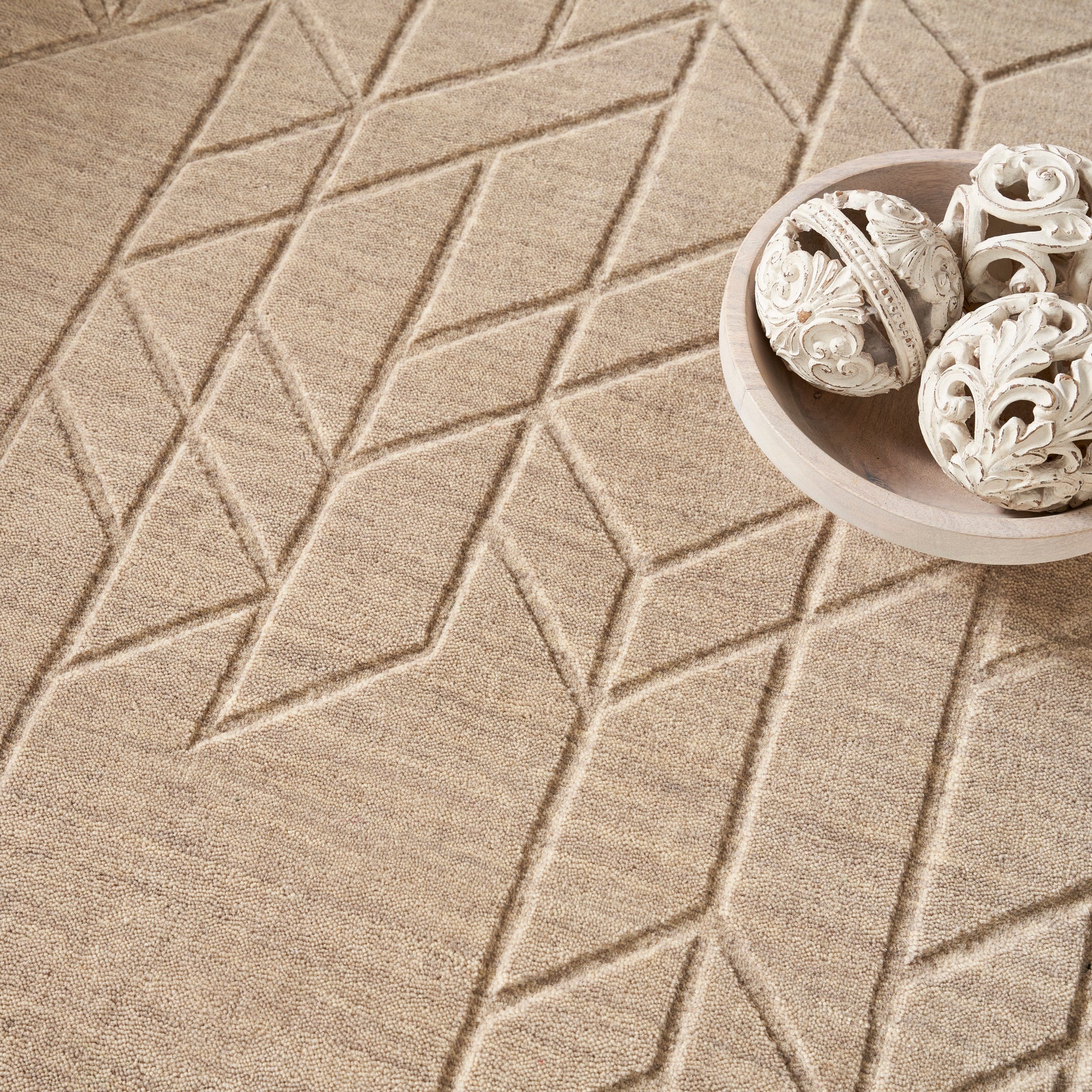 Beige geometric rug with raised diamond pattern; round light wood bowl containing white carved ornamental spheres.