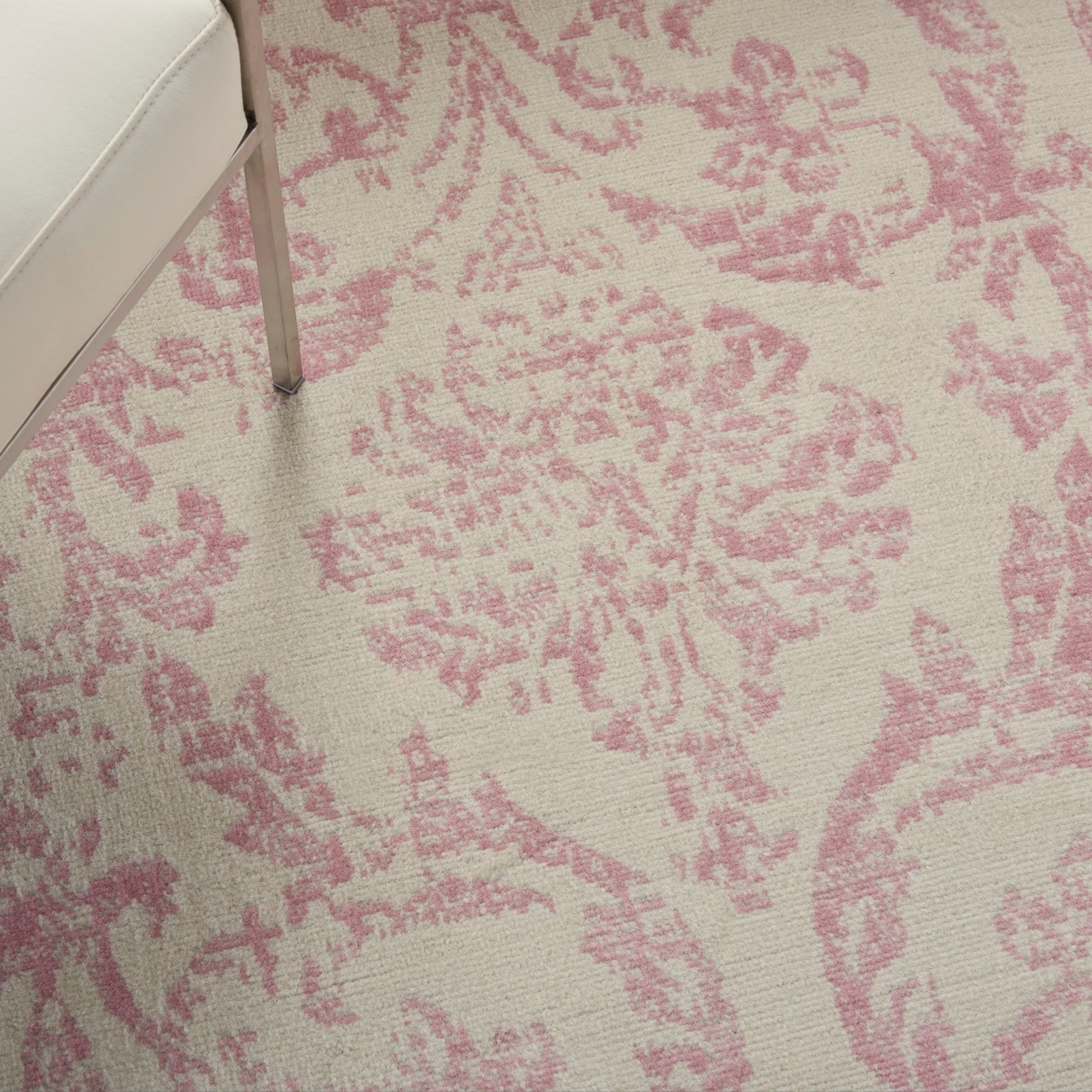 Beige area rug with pink damask floral pattern; white sofa with metal leg partially visible.