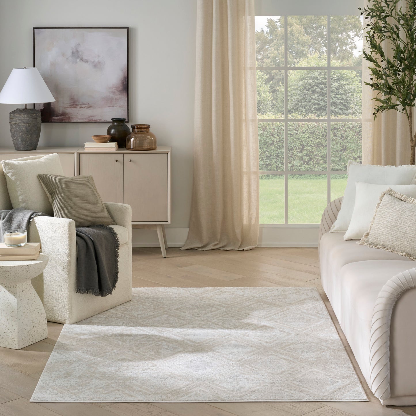 Neutral living room with cream sofa, white armchair, light wood sideboard, ceramic vases, beige patterned rug, and large window with cream curtains.