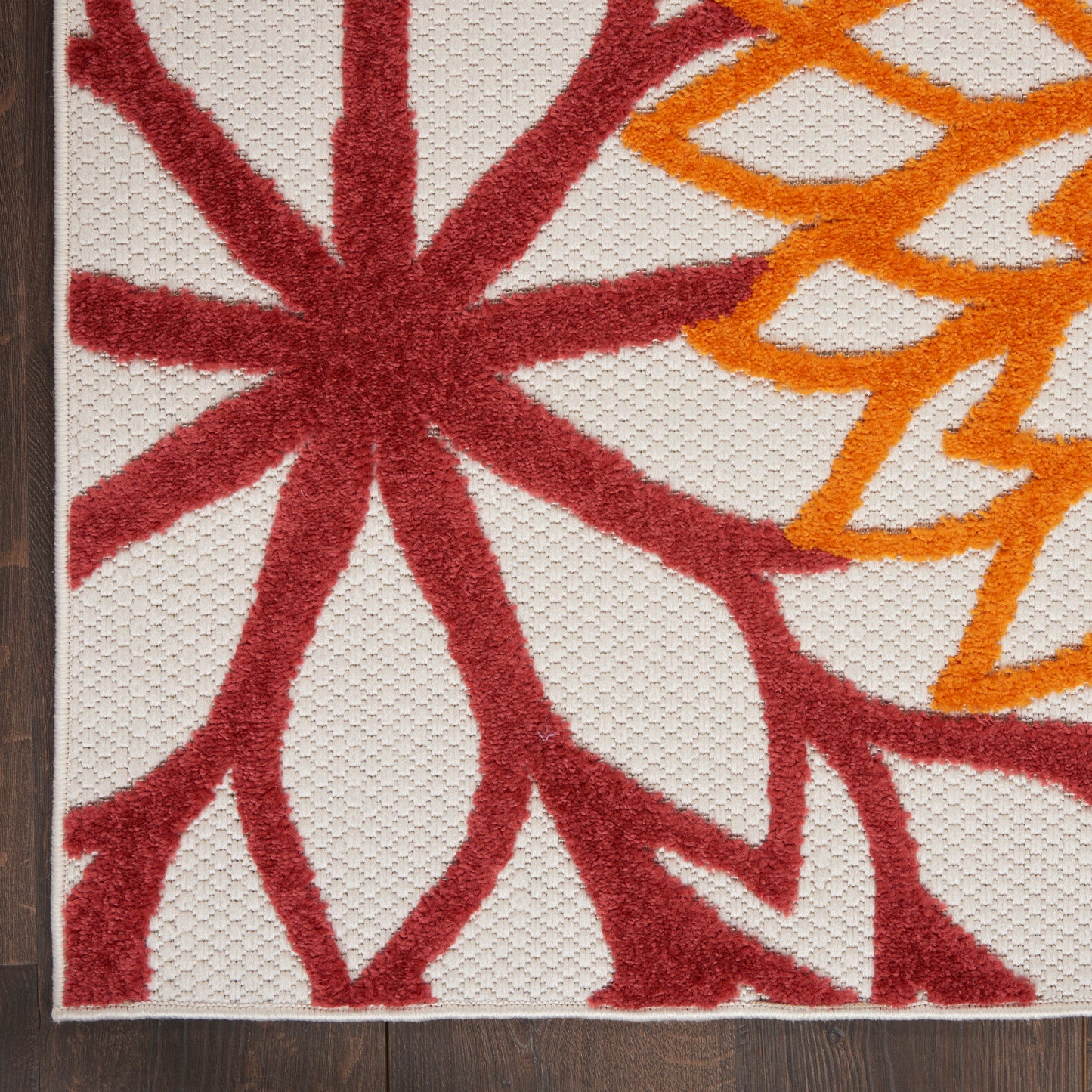 Beige area rug with bold red starburst and orange curls, textured pile, white border, on dark wood floor, 3' x 5'.
