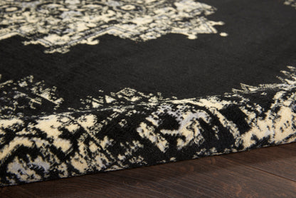 Black round rug with ivory damask pattern, folded edge on dark wood floor.
