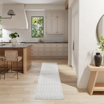 Gray geometric-patterned runner rug in bright modern kitchen with light wood floor, island, and white cabinets.