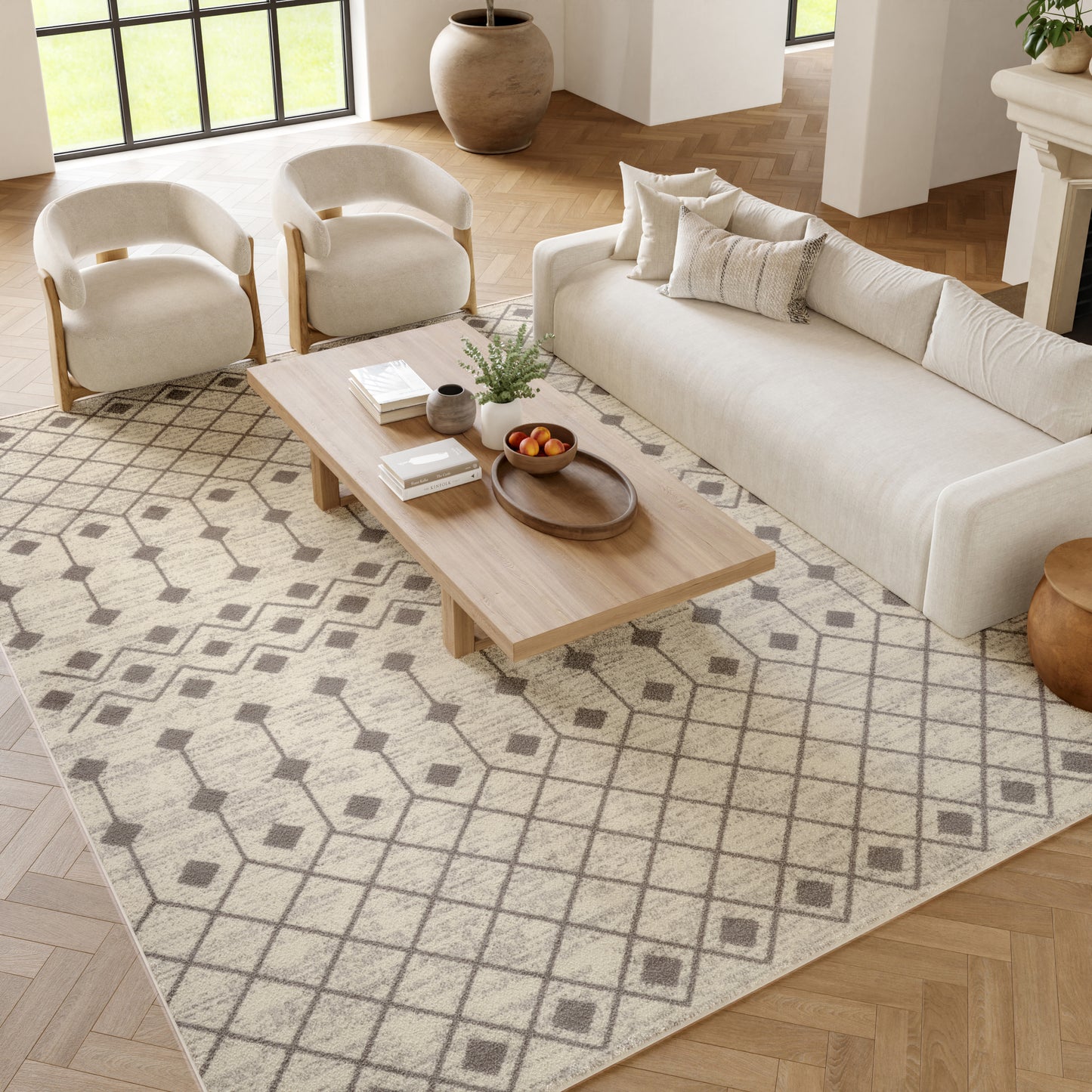 Neutral living room: cream sofa and curved wooden-frame armchairs, light wood coffee table on a geometric beige rug.