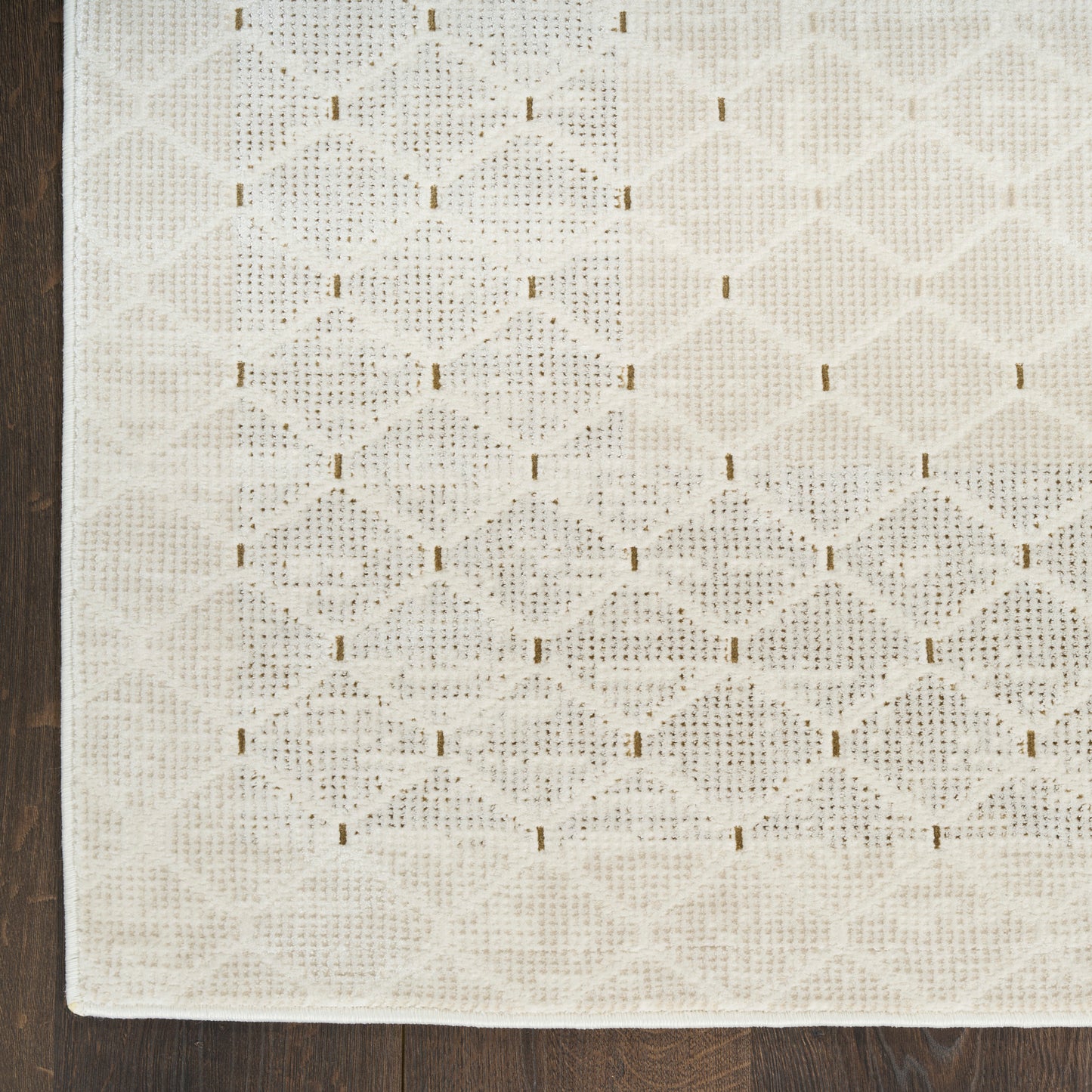 Ivory lace-style area rug with diamond lattice crochet pattern and tiny gold-tone rectangular accents; on dark wood floor.