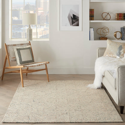 Neutral living room with light wood lounge chair, patterned cushions, cream rug, fluffy throw on grey sofa, geometric art.