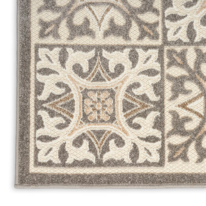 Corner view of a beige and gray tufted rug with ornate damask floral pattern and thick border.