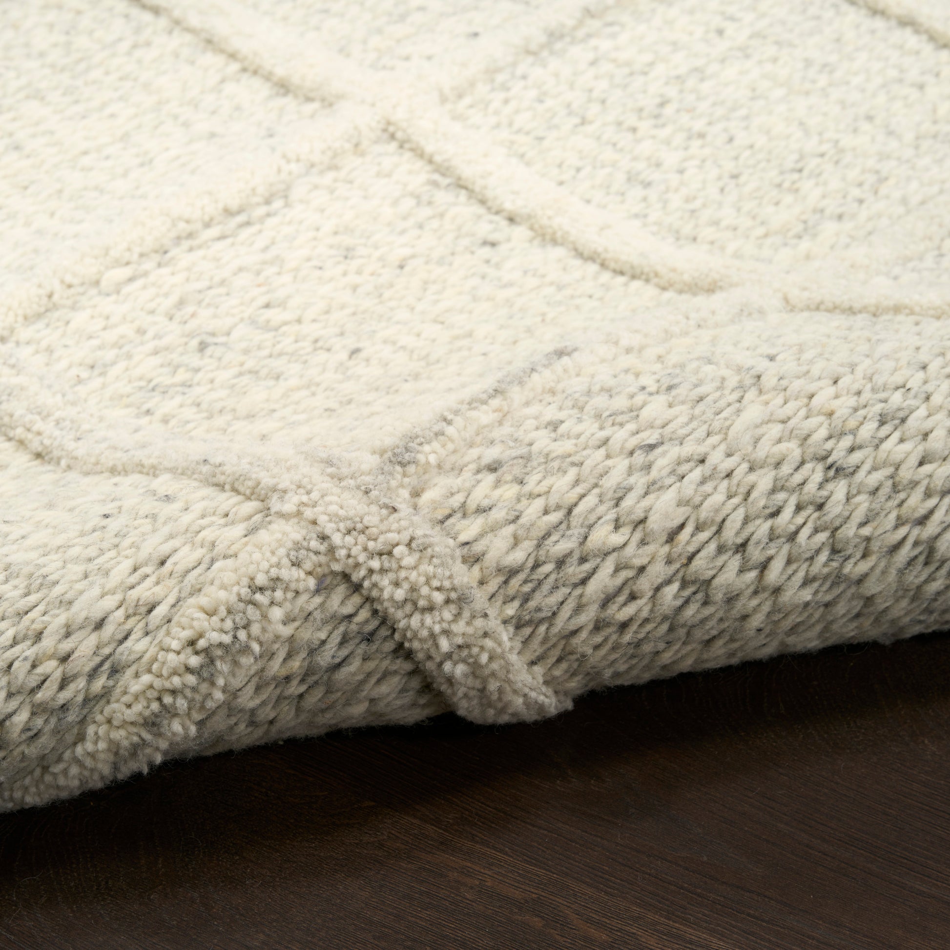 Cream textured area rug with a geometric square pattern; plush looped pile, folded edge on dark wooden floor.