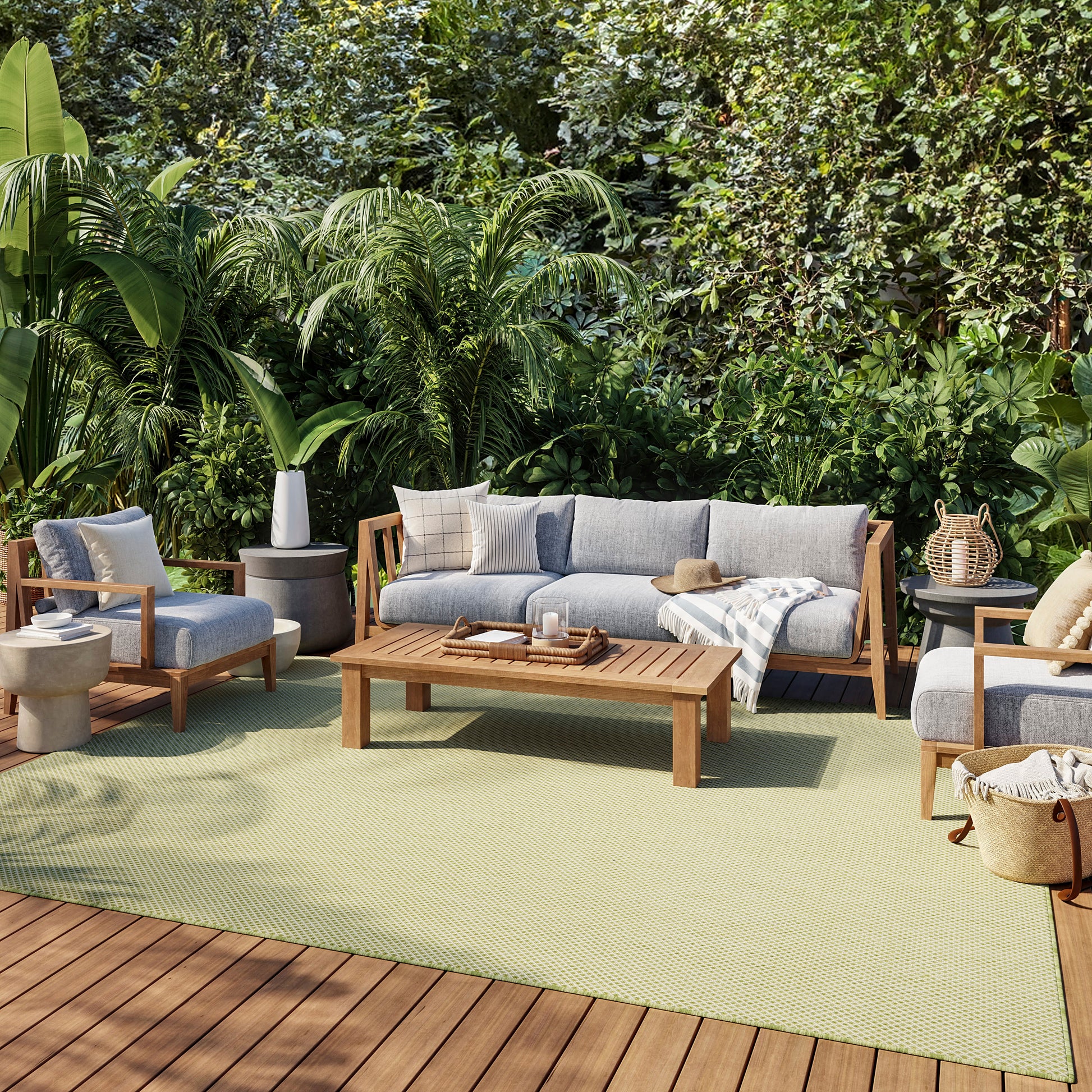 Outdoor wooden-frame sofa and chairs with gray cushions, coffee table, beige throw, on a light green rug amid lush greenery.