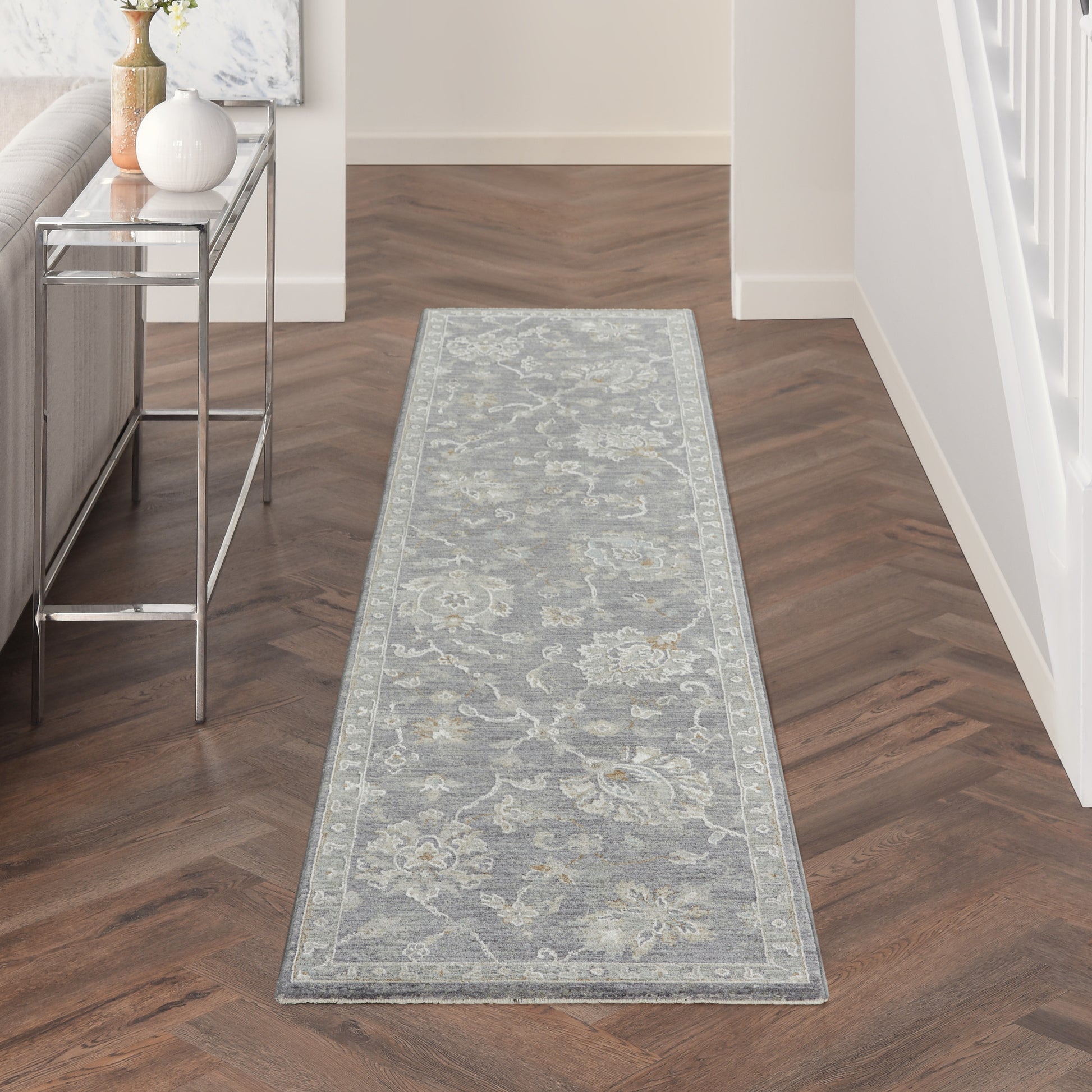 Blue-gray floral runner rug with pale border on dark herringbone hallway floor, beside a glass-top console.