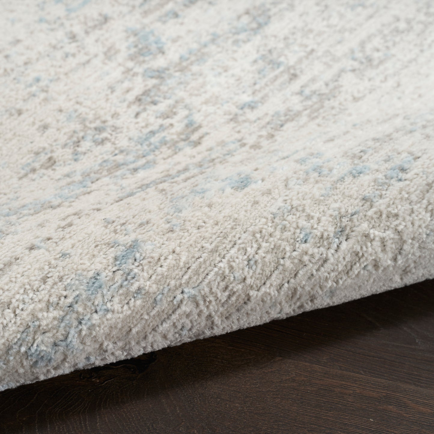 Cream shag rug with subtle pale blue pattern, plush texture on dark wood floor.