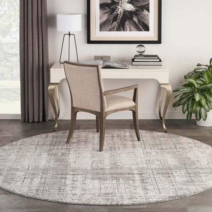 Beige upholstered desk chair with wooden frame at a white desk, round gray patterned rug, lamp, plant and framed art.