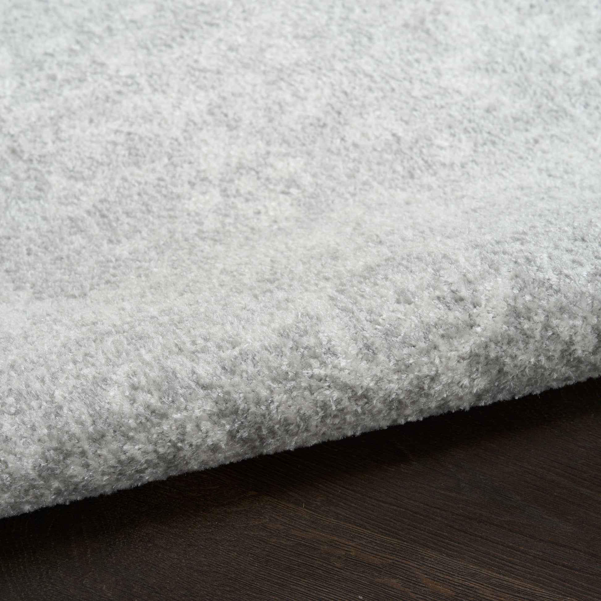 Light gray plush shag rug with thick pile and folded edge on dark wood floor.