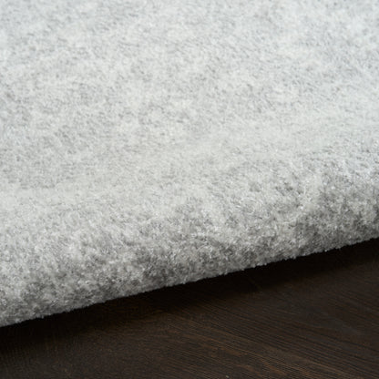 Light gray plush shag rug with thick pile and folded edge on dark wood floor.