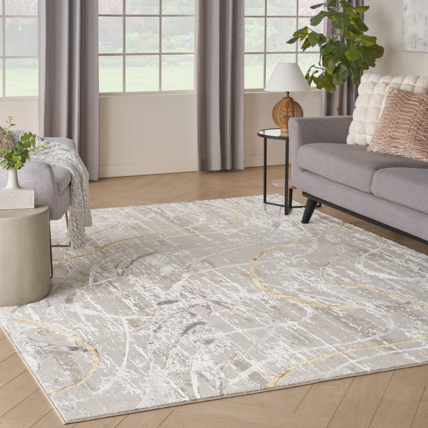 Abstract cream-gray rug with white and gold curves on a light wood floor in a modern living room with gray sofa.