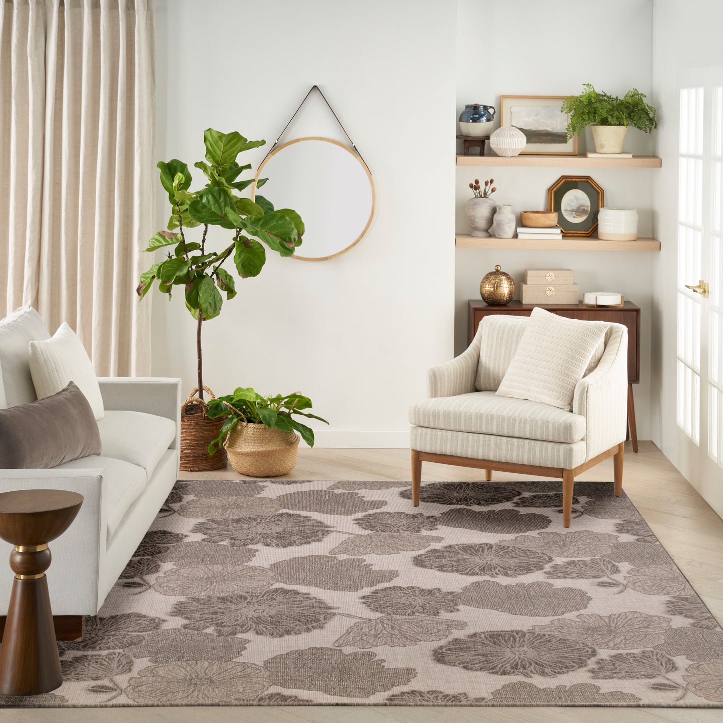Neutral living room with cream sofa, striped armchair, large floral rug, fiddle-leaf fig in woven basket, round wall hoop.
