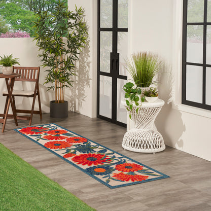 Long floral runner rug with bright red-orange flowers and blue border beside potted plants and black-framed glass doors.