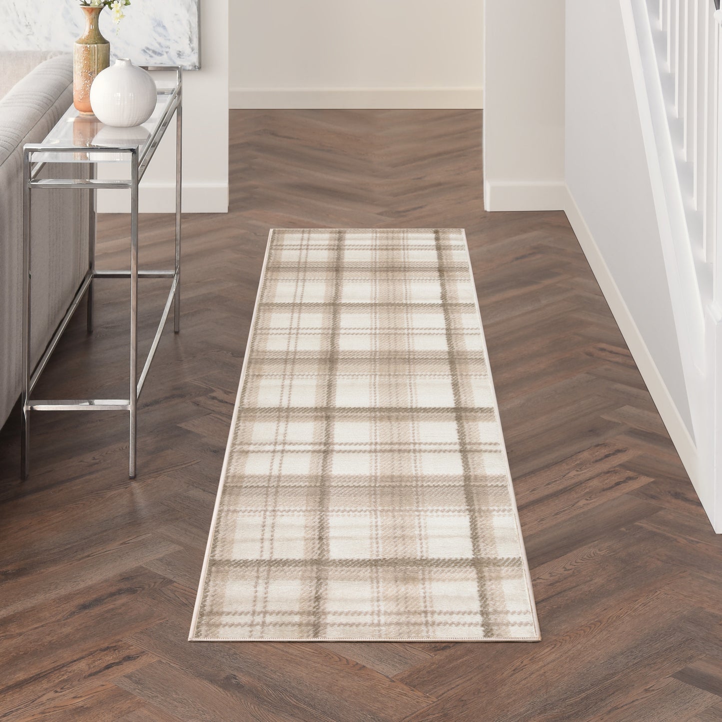 Beige plaid hallway runner rug on dark wood herringbone floor with a chrome-framed console table and neutral decor.