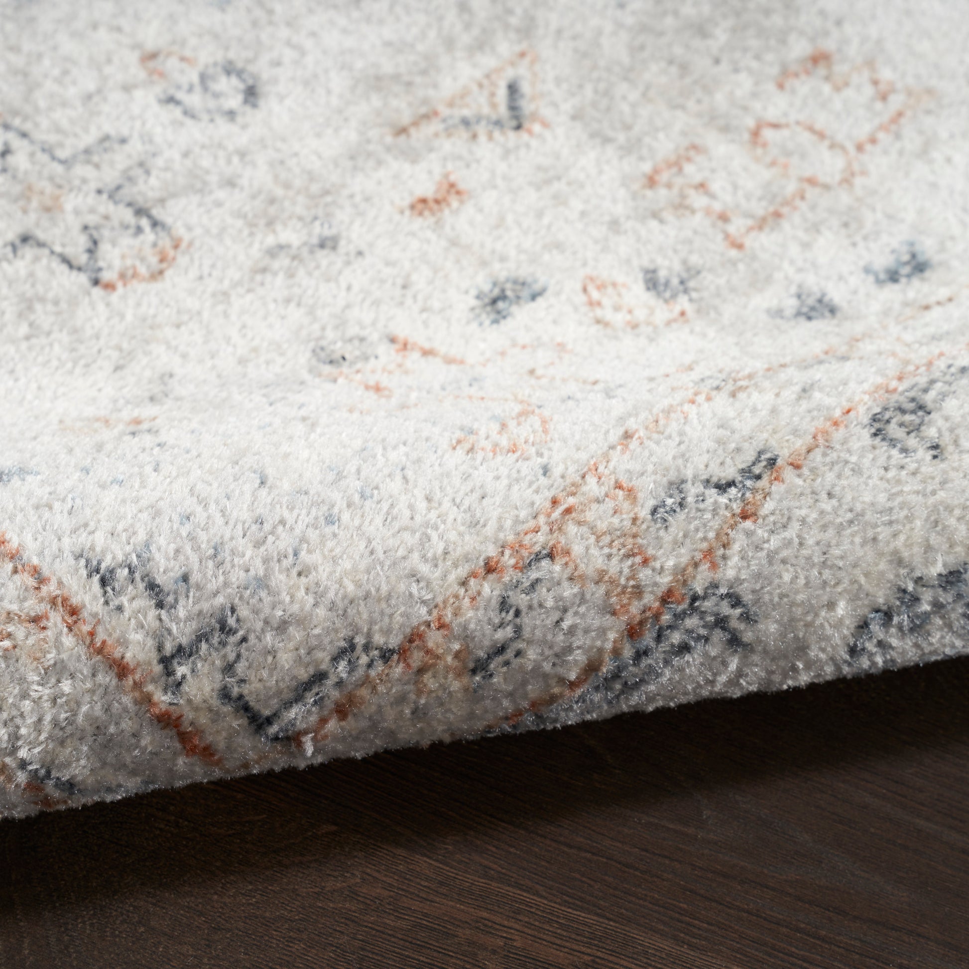 Soft light-gray rug with orange and blue geometric accents, plush pile, resting on dark wooden floor.