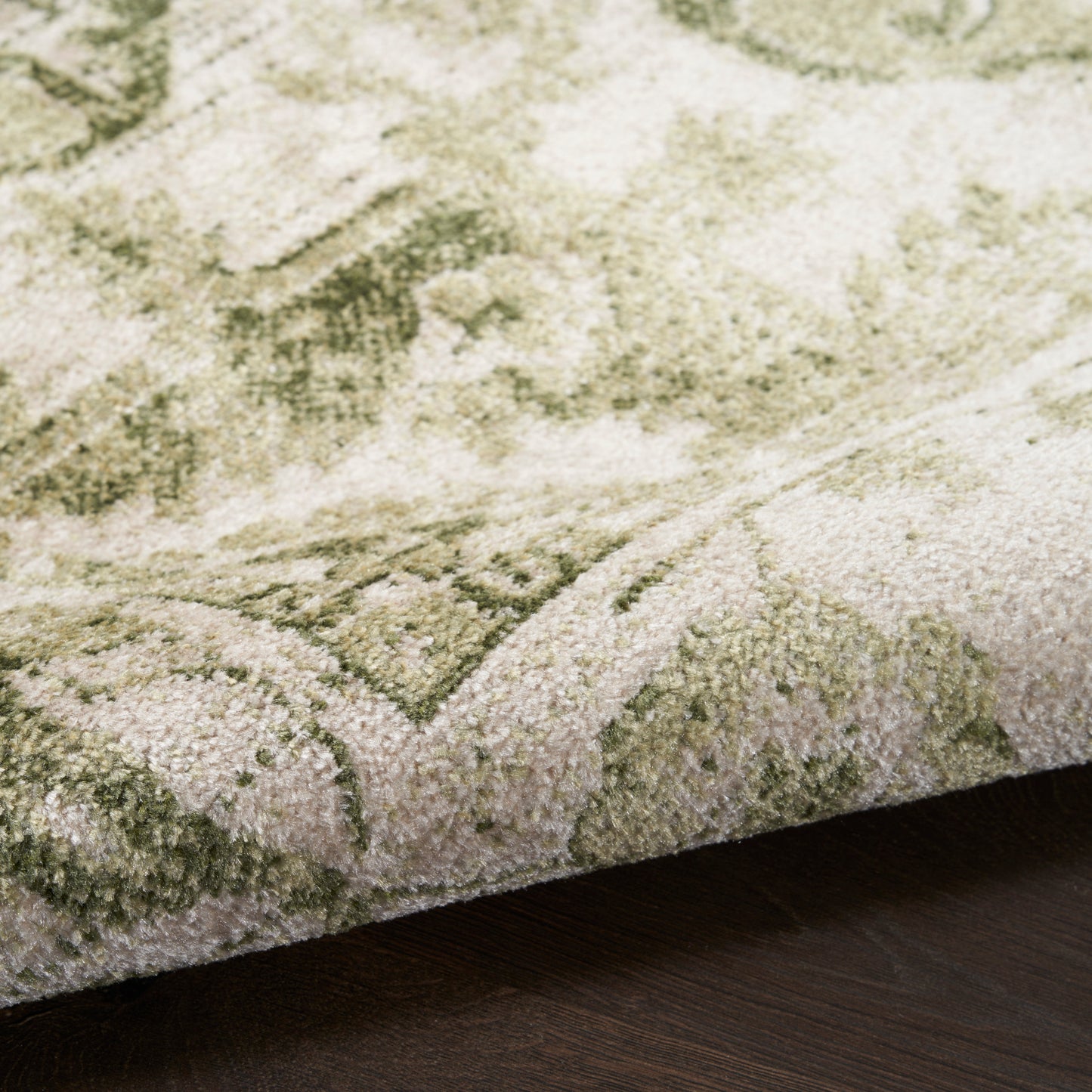 Close-up of sage green and ivory oriental-style rug with plush pile, folded edge on dark wood floor