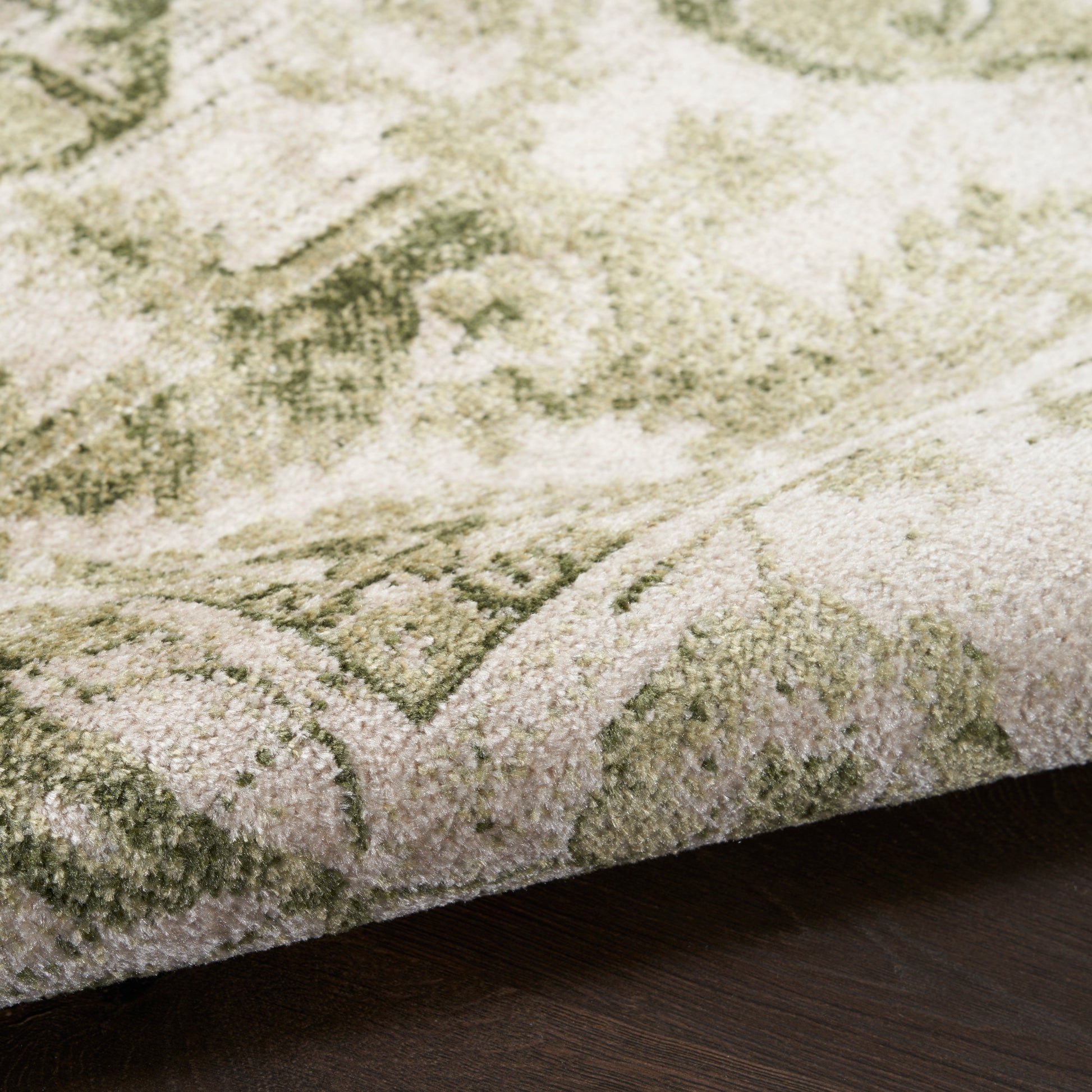 Close-up of sage green and ivory oriental-style rug with plush pile, folded edge on dark wood floor