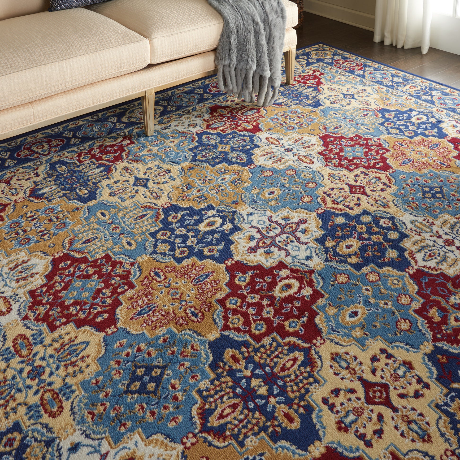 Multicolor ornate area rug with blue, red, gold floral medallions under a beige sofa and gray throw.