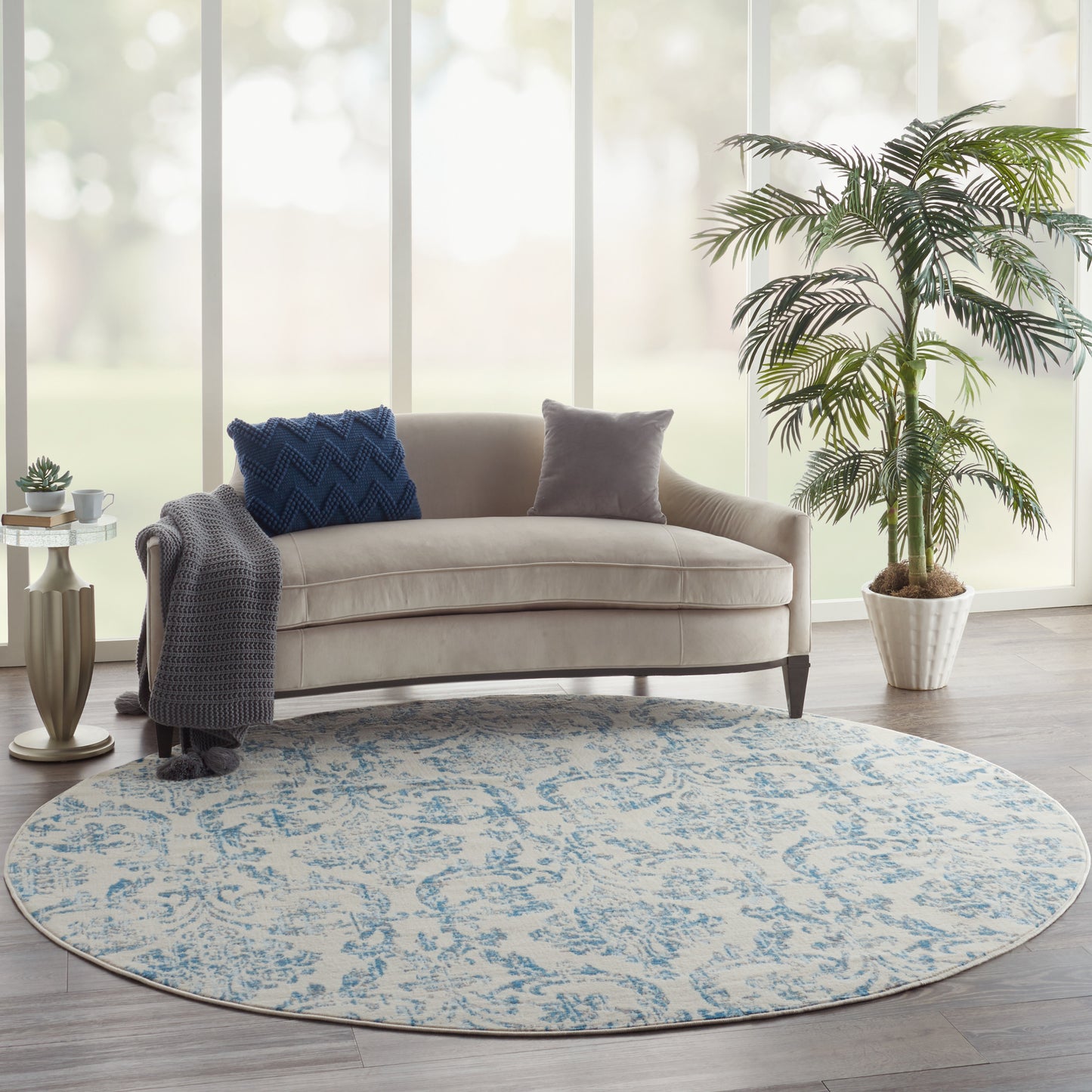 Round blue-and-cream patterned rug under a beige curved sofa with blue throw pillow and gray pillow, modern living room.