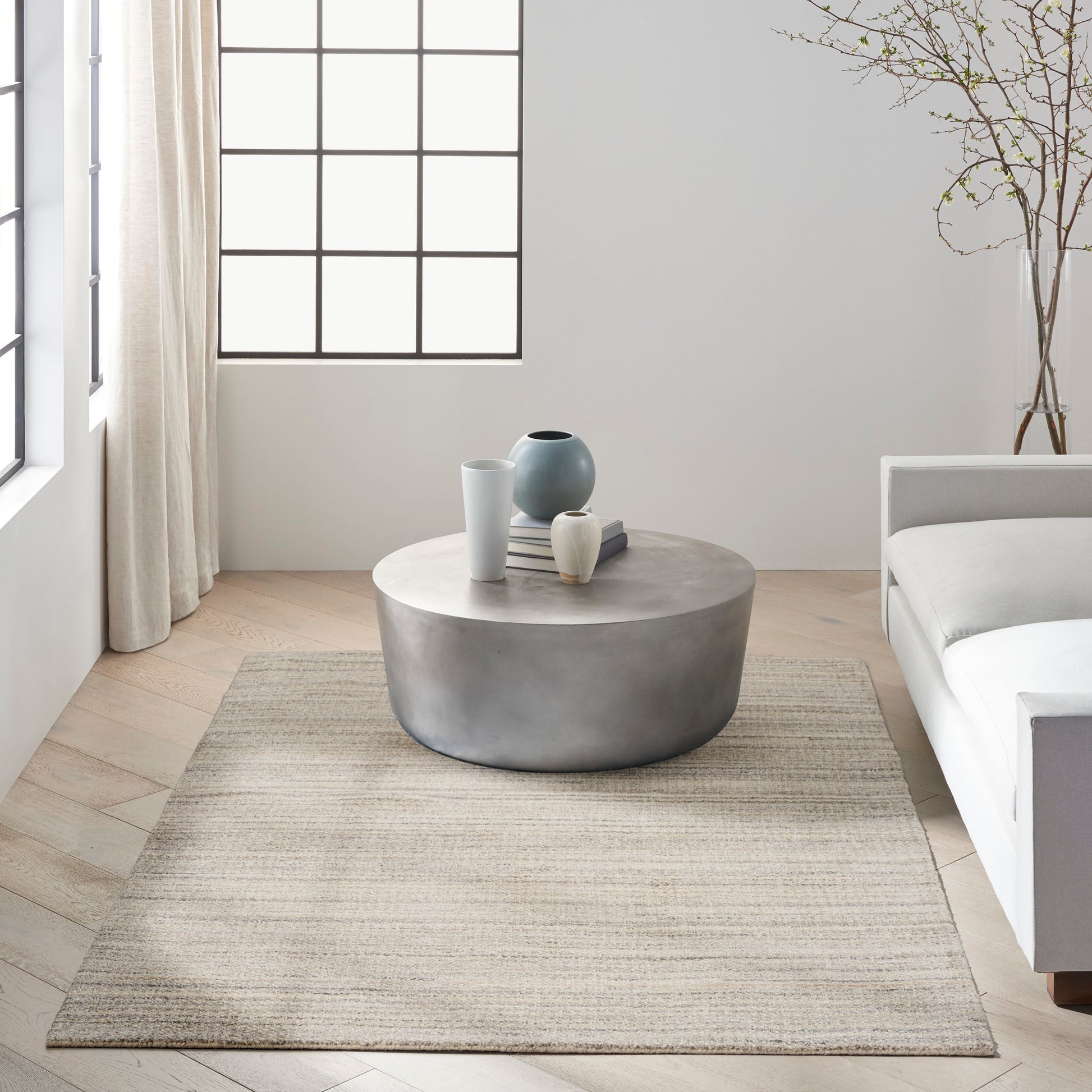 Minimalist living room with round concrete coffee table, ceramic vases, beige rug, grid-window, white sofa.