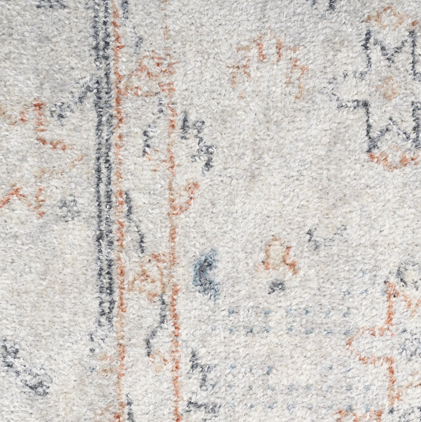 Beige plush rug close-up with blue and orange abstract motifs and a dark vertical line.