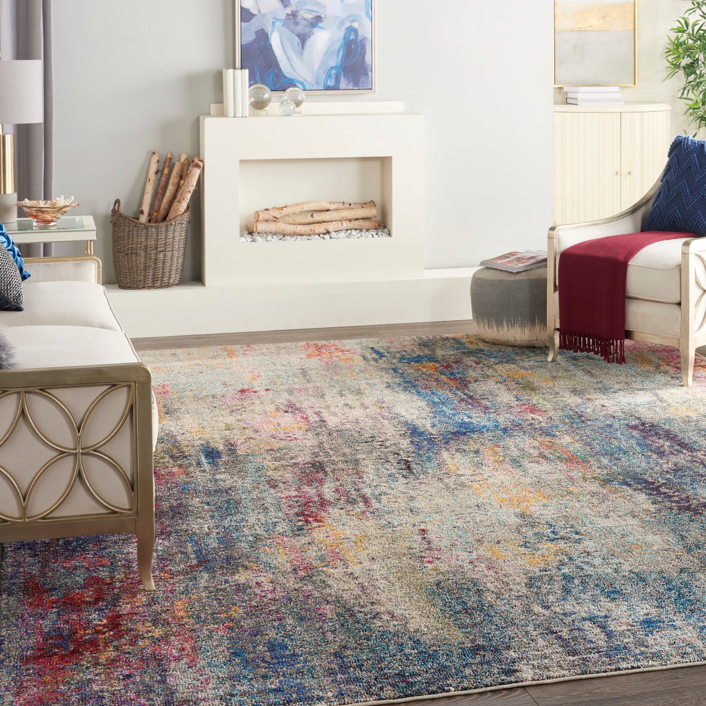 Living room with colorful abstract rug, white fireplace, beige metal-frame sofa, and cream armchair with burgundy throw.