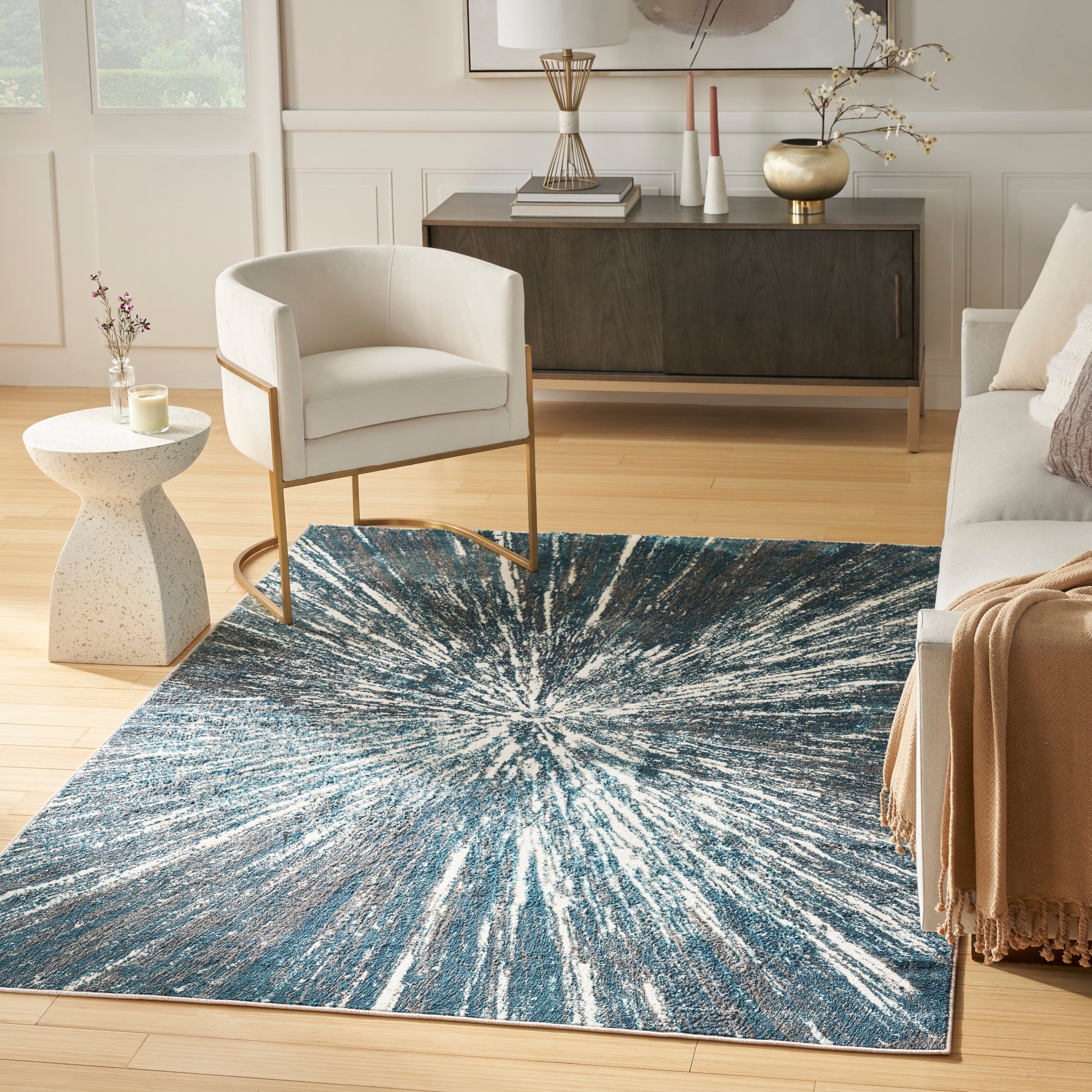 Blue starburst rug on light wood floor, white armchair with wood legs, beige walls, mid-century living room.
